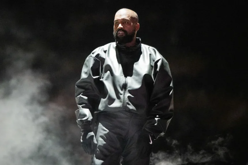 Kanye West standing on stage in a grey Nike tracksuit surrounded by smoke during the Bully album listening event