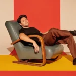 Niall Horan seated in a vintage leather chair against a bold red and yellow backdrop.