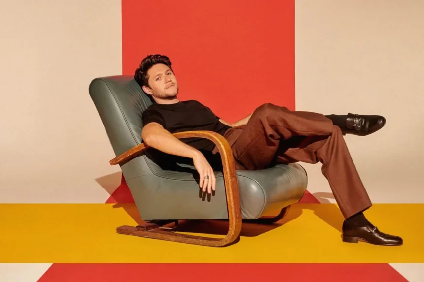 Niall Horan seated in a vintage leather chair against a bold red and yellow backdrop.