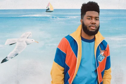 Singer Khalid wearing a colorful Gucci track jacket, posed in front of an ocean mural.