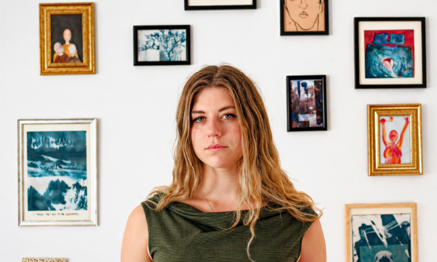 Ella Clayton standing before a gallery wall of framed artwork, promoting her second album 'Could It Be You?'