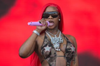 Sexyy Red performing live with a pink microphone, wearing her signature 'Big Sexyy' chain and red hair, promoting her 2026 album 'Yo Favorite Trappa Favorite Rappa'