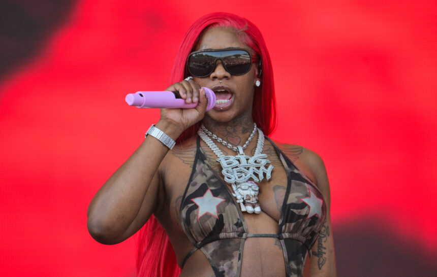 Sexyy Red performing live with a pink microphone, wearing her signature 'Big Sexyy' chain and red hair, promoting her 2026 album 'Yo Favorite Trappa Favorite Rappa'