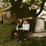 Alt-rock trio thistle. posed together in a moody, low-lit portrait, photographed by Briony Graham-Rudd
