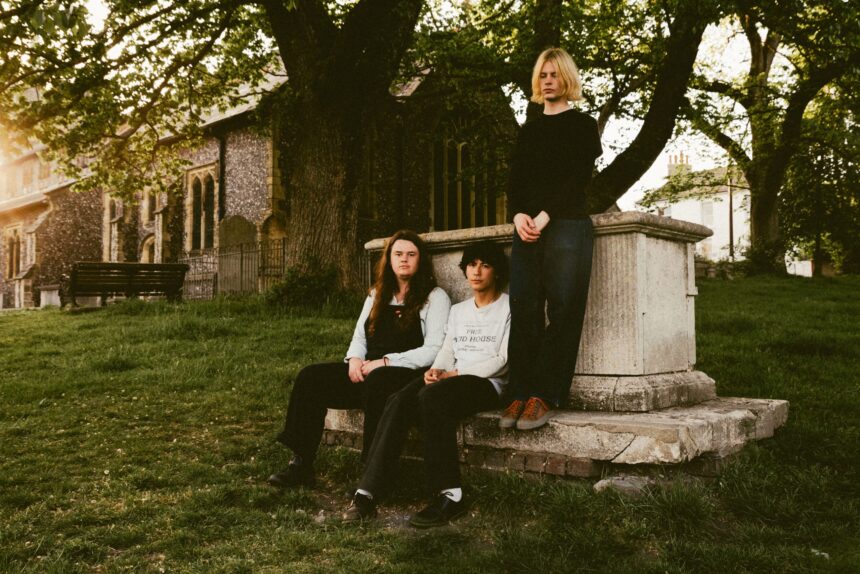 Alt-rock trio thistle. posed together in a moody, low-lit portrait, photographed by Briony Graham-Rudd
