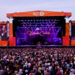 Belinda Carlisle performing on the BBC Radio 2 main stage at Radio 2 in the Park, with a large crowd in the foreground and giant LED screens displaying her image