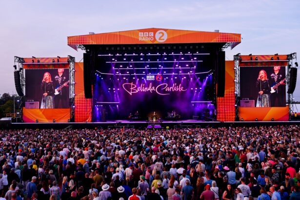 Belinda Carlisle performing on the BBC Radio 2 main stage at Radio 2 in the Park, with a large crowd in the foreground and giant LED screens displaying her image