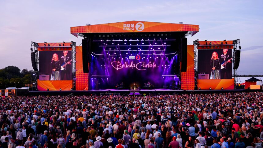 Belinda Carlisle performing on the BBC Radio 2 main stage at Radio 2 in the Park, with a large crowd in the foreground and giant LED screens displaying her image