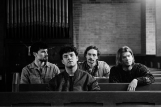 Basht sit in a dim, church-like space as they announce their debut album Poor Advice, arriving in October, alongside the lead single “Perfume.”