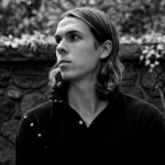 Black and white portrait of Loukeman against a stone wall.