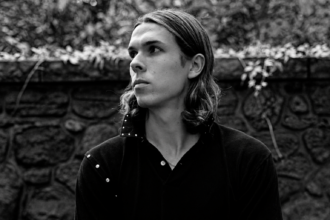 Black and white portrait of Loukeman against a stone wall.