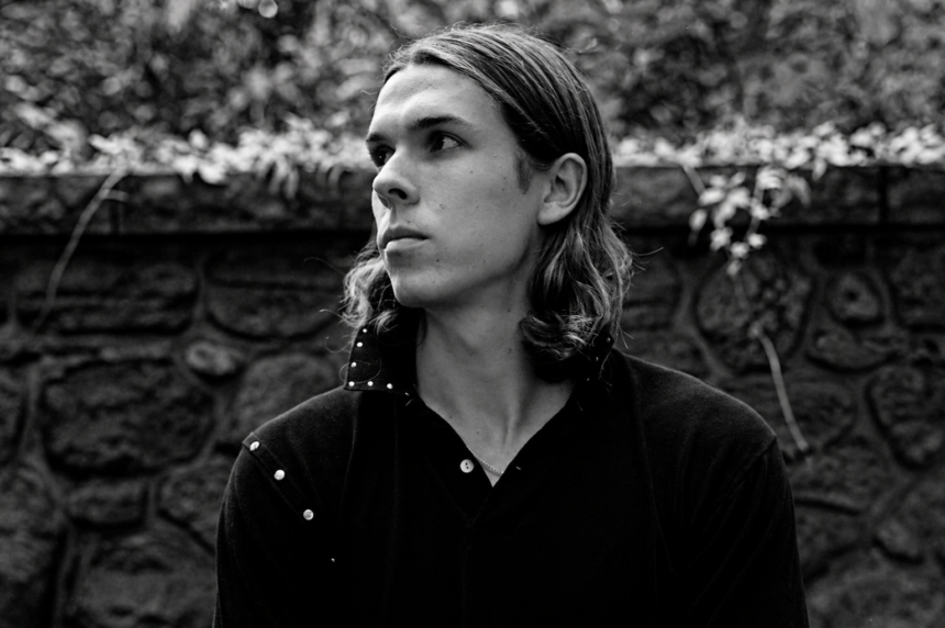 Black and white portrait of Loukeman against a stone wall.