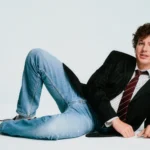 Charlie Puth poses casually on a white studio floor promoting his 2026 Whatever's Clever! World Tour