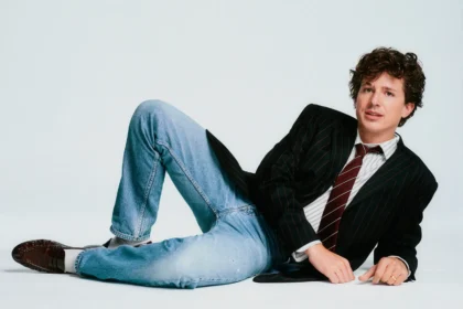Charlie Puth poses casually on a white studio floor promoting his 2026 Whatever's Clever! World Tour