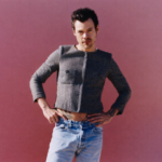 Harry Styles Man posing confidently against a pink background, wearing a cropped jacket and jeans