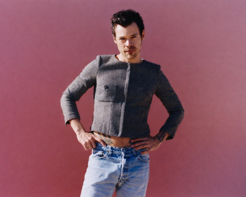 Harry Styles Man posing confidently against a pink background, wearing a cropped jacket and jeans