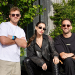 Lauren Mia and MAMI photographed together at a festival, the trio posing in front of a lush green wall