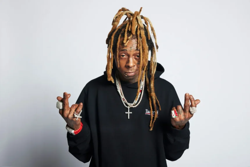Lil Wayne posing in a black hoodie with diamond chains, rings, and his signature blonde dreadlock