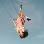 Olivia Rodrigo upside down on a swing in a pink dress against a blue sky, official album cover for 'You Seem Pretty Sad for a Girl So in Love'