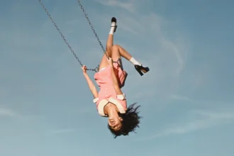 Olivia Rodrigo upside down on a swing in a pink dress against a blue sky, official album cover for 'You Seem Pretty Sad for a Girl So in Love'