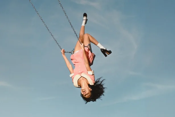 Olivia Rodrigo upside down on a swing in a pink dress against a blue sky, official album cover for 'You Seem Pretty Sad for a Girl So in Love'