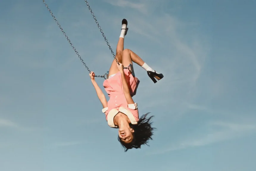 Olivia Rodrigo upside down on a swing in a pink dress against a blue sky, official album cover for 'You Seem Pretty Sad for a Girl So in Love'