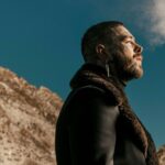 Post Malone in side profile against a rocky mountain backdrop and blue sky - LateTown jpg