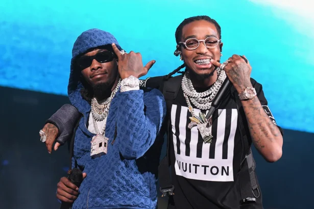 Offset and Quavo of Migos performing on stage, wearing diamond chains and designer outfits, holding microphones.