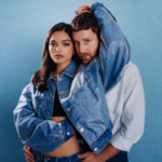 Rachel Zegler and Ben Platt pose together in matching denim jackets against a blue background for The Last Five Years 25th Anniversary live album press photo