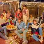 SEVENTEEN's 13 members pose together in a rooftop setting decorated with string lights.