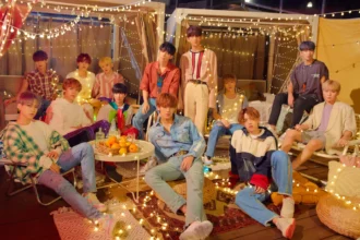 SEVENTEEN's 13 members pose together in a rooftop setting decorated with string lights.
