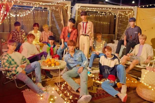 SEVENTEEN's 13 members pose together in a rooftop setting decorated with string lights.