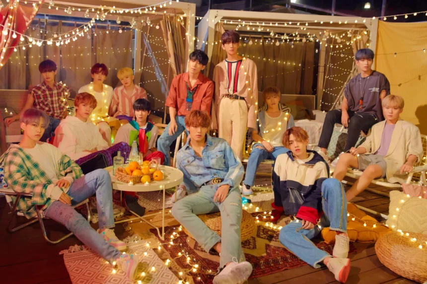 SEVENTEEN's 13 members pose together in a rooftop setting decorated with string lights.