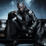 Skepta sits on a dark leather couch wearing an all-black leather outfit and gloves LateTown