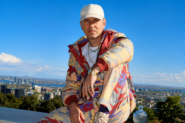 Tiga, Montreal DJ and producer, posing against the Montreal city skyline in a patterned jacket and white cap, promoting his 2026 album 'HOTLIFE'
