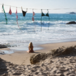 Woman sitting on SoCal beach with bikinis hanging on a clothesline by the ocean