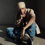 **Alt text:** 6LACK sits on the floor in a relaxed pose against a neutral studio backdrop, wearing a white bandana, beige shirt, and distressed jeans, in a press photo for his 2026 "10 Years of 6LACK" world tour.