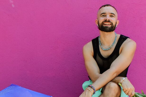 Olof Dreijer press photo against a pink wall, smiling in a black mesh top and layered jewelry