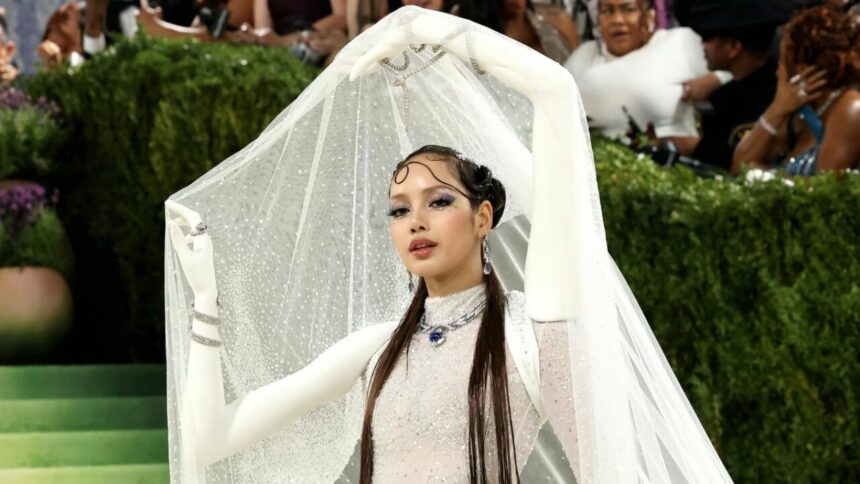 Lisa attends the Met Gala 2026 in a sparkling white couture gown with long gloves and a dramatic crystal veil, posing on the red carpet in an avant-garde fashion look.