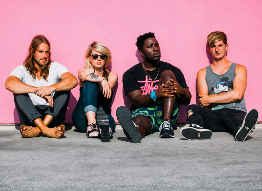 Bloc Party's four members seated casually against a bright pink wall in an outdoor promotional photo shoot