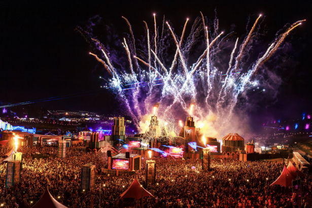 Boomtown Fair 2026 night aerial view showing fireworks, fire effects, and a massive crowd gathered around illuminated stage structures at Matterley Estate, Hampshire, UK