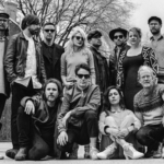 Broken Social Scene band photo, a large group of roughly a dozen musicians posed together outdoors in a parking lot or schoolyard, shot in black and white