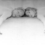 Dancing In Tongues press photo — black and white image of two people lying side by side, heads touching, arms extended, looking directly into the camera