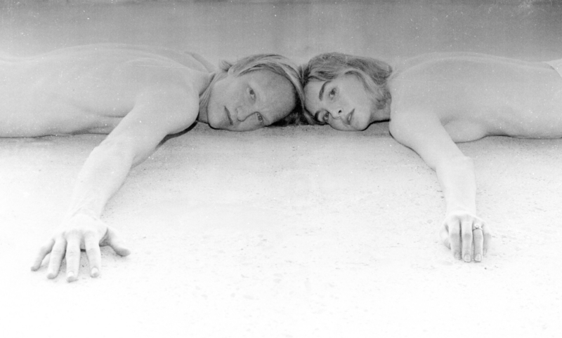 Dancing In Tongues press photo — black and white image of two people lying side by side, heads touching, arms extended, looking directly into the camera