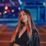 `Emily Brooks poses on a nighttime LA street in a black leather jacket, in a press photo for her new single 'Black Cat.'`
