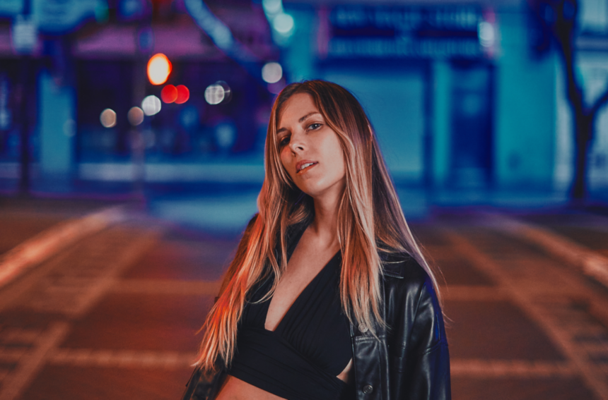 `Emily Brooks poses on a nighttime LA street in a black leather jacket, in a press photo for her new single 'Black Cat.'`