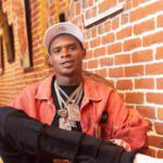 `HoodTrophy Bino rapper wearing orange jacket and gold chains promoting new album Made A Way 2026`
