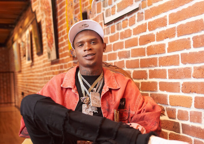 `HoodTrophy Bino rapper wearing orange jacket and gold chains promoting new album Made A Way 2026`