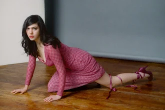 Julia Cumming in a pink lace mini dress, posing on a hardwood floor. Photo by Marcus Maddox