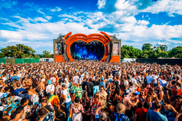 `Crowds fill the main stage arena at Love Saves The Day festival in Bristol, with the iconic heart-shaped orange stage structure under a bright summer sky.`